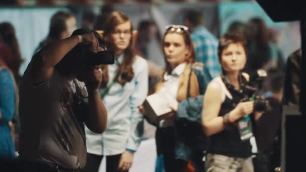 SAINT PETERSBURG, RUSIA - 20 DE MAYO DE 2017: El hombre gordo fotógrafo en gorra de béisbol toma fotos en el salón lleno de gente — Vídeos de Stock