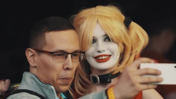 SAINT PETERSBURG, RUSSIA - MAY 20, 2017: Young man in glasses takes selfie with girl in Harley Quinn character costume — Stock Video