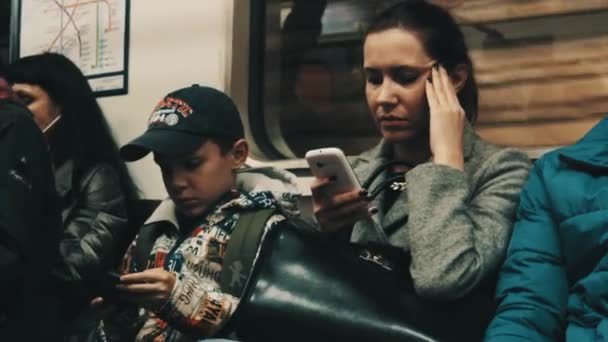 Petersburg, Rosja - 30 września 2016: Kobieta z migrena i chłopak w czapce za pomocą smartfonów, siedzi w pociągu metra — Wideo stockowe
