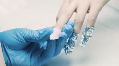 Manikürcü el gümüş folyo parça istemci parmak çevresinde salonda koyar.