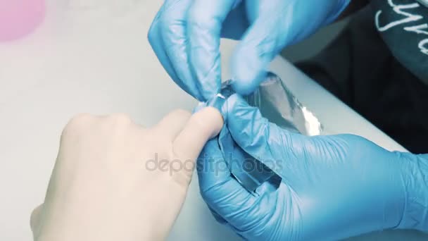 Schoonheidsspecialist hand zet zilver folie stuk rond client vinger in salon — Stockvideo