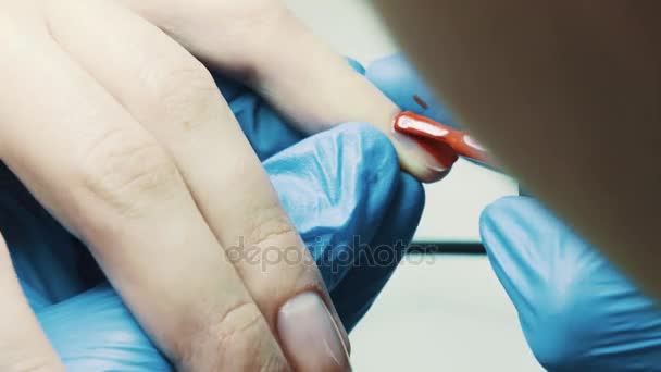 La mano esteticista pone esmalte de uñas rojo en la uña del pulgar del cliente en el salón — Vídeos de Stock