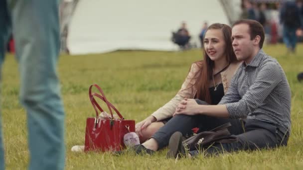 SAINT PETERSBURG, RÚSSIA - JUNHO 24, 2017: Jovem casal sentado na grama assistindo ao desempenho no verão evento ao ar livre — Vídeo de Stock