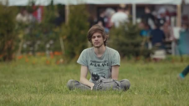 SAINT PETERSBURG, RÚSSIA - JUNHO 24, 2017: Jovem homem desajeitado sentado na grama no festival ao ar livre de verão — Vídeo de Stock