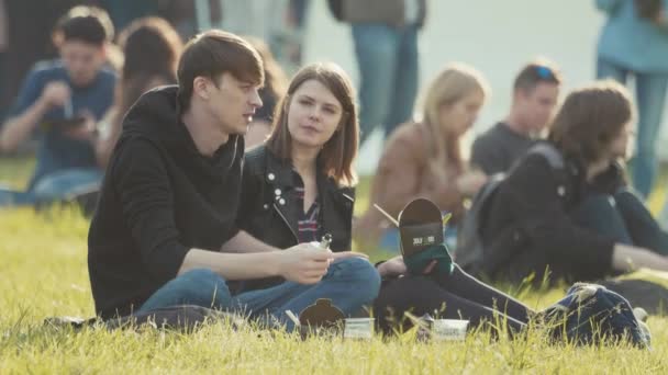 SAINT PETERSBURG, RÚSSIA - JUNHO 24, 2017: Casal jovem sentado na grama, conversando no festival. Homem fumando vape — Vídeo de Stock