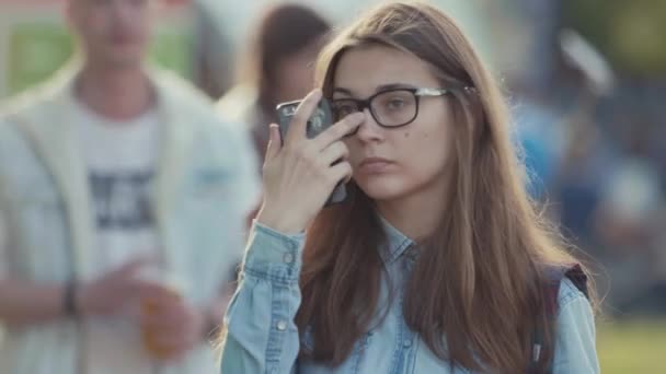 SAINT PETERSBURG, RUSSIE - 24 JUIN 2017 : Une jeune fille mignonne aux lunettes cassées tient un téléphone intelligent dans un parc urbain bondé — Video