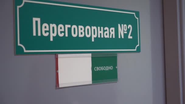 La mano de la mujer mueve la placa a ocupada en la puerta con la sala de reuniones de texto cirílico — Vídeo de stock
