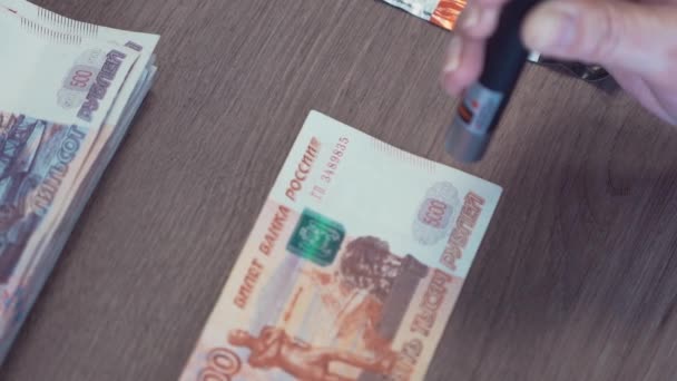 Mano femminile con laser per controllare cinquemila banconote in rublo sul tavolo — Video Stock