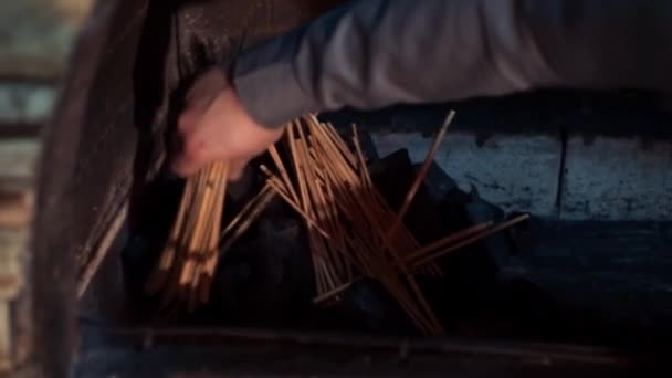 Чоловіча рука кладе дерев'яні палички для розкладання на вугільну купу в каміні — стокове відео