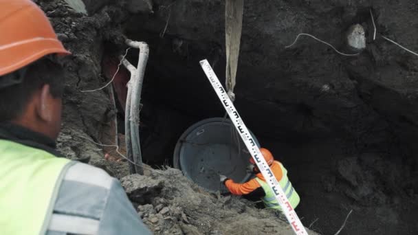 Trabajador en naranja casco de sombrero duro hasta anillo de alcantarilla de cámara de hormigón en cadenas — Vídeos de Stock