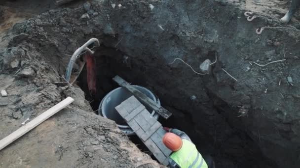 Worker in hard hat put platform on concrete chamber manhole ring in ditch — Stock Video