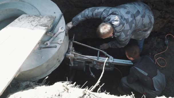 Dos hombres taladran agujero circular en anillo de alcantarilla de hormigón usando taladro industrial — Vídeos de Stock