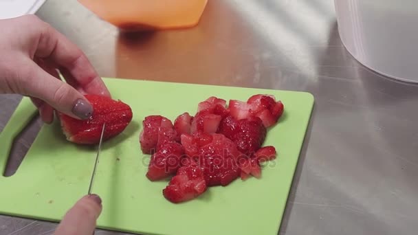 Frauenhände schnitzen Erdbeere auf Schneidebrett in Küche auf Metalltisch — Stockvideo