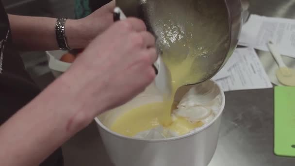 Female confectioner puts whipped egg yolk into mixing bowl with whipped cream — Stock Video