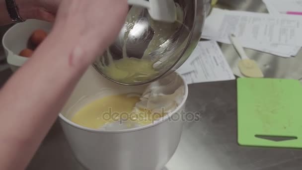 Woman pastry cook puts whipped egg yolk into mixing bowl with whipped cream — Stock Video