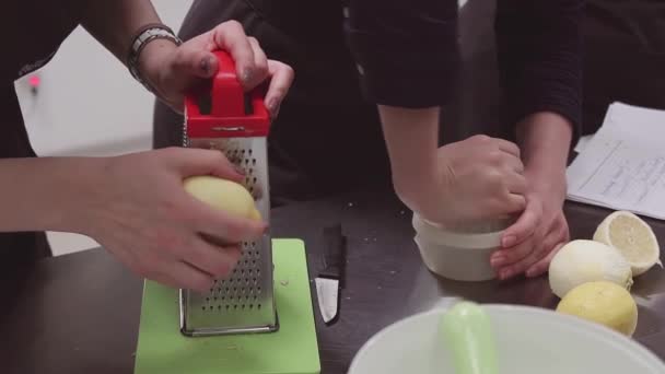 Женщины готовят в фартуках с помощью терки и соковыжималки с лимонами за кухонным столом — стоковое видео