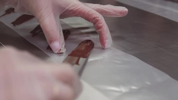 Woman confectioner hands in plastic gloves puts chocolate on cooking strip — Stock Video