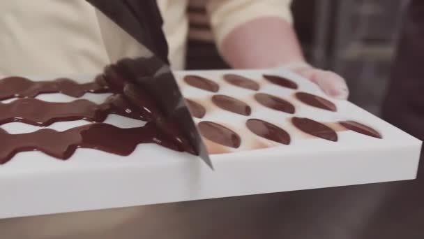 Кондитер соскребает излишний шоколад с пластиковой плесени — стоковое видео