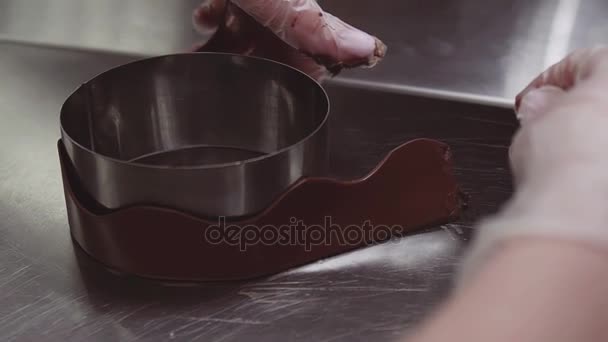 Mãos de confeiteiro envolve decoração de chocolate em torno de assadeira de metal — Vídeo de Stock