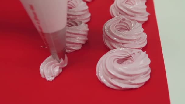 Fazer bolos merengues espremendo saco de pastelaria na superfície de cozimento vermelho — Vídeo de Stock