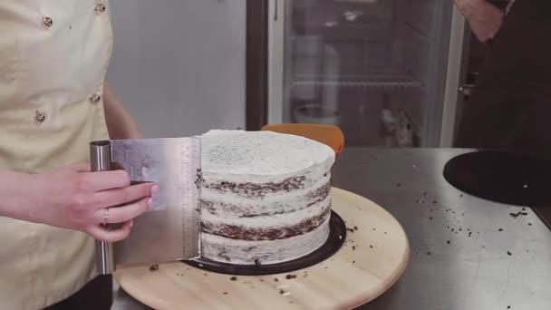 Woman confectioner using pastry scraper to take excessive cream of cake — Stock Video