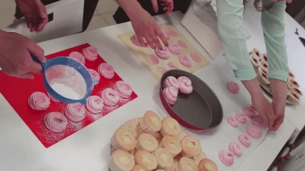 El confitero femenino en delantal tamiza el azúcar en polvo a través del cedazo en los merengues — Vídeo de stock