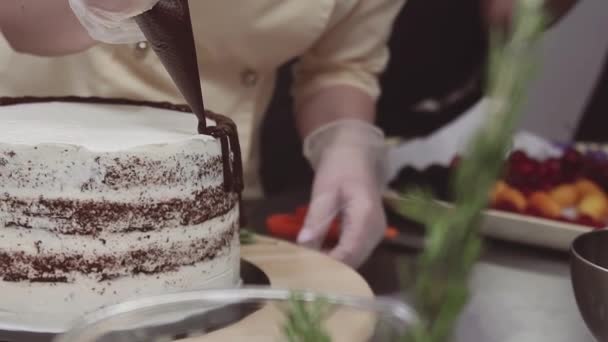 Женщина-кондитер украшает бисквитный торт расплавленной шоколадкой — стоковое видео