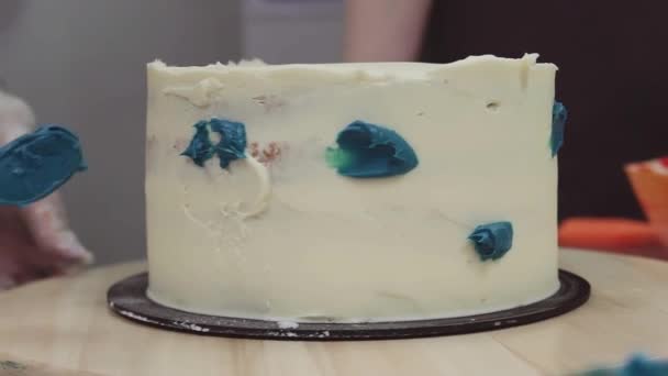 Konditor schmiert von Hand blaue Creme auf weiße Sahne mit Zuckerguss — Stockvideo