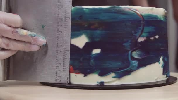 Chef pastelero manos suavizar azul colorido glaseado en la torta usando raspador de pastelería — Vídeo de stock