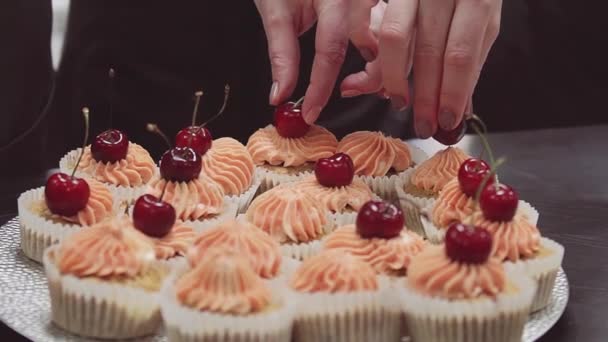 Cukrář ruce zdobí muffiny krém topy s cherry bobule — Stock video