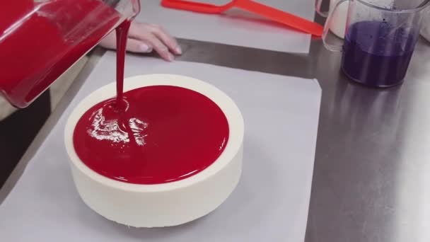 Confectioner pours red mirror glaze icing on cake from measuring cup — Stock Video