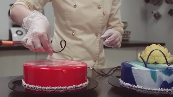 Кондитер украшает красное зеркало глазурью торт с шоколадной полосой вихря — стоковое видео