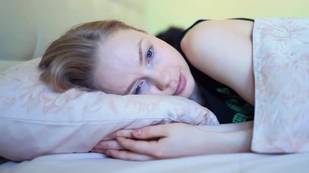 Jonge vrouw met blauwe ogen glimlachend in bed na het ontwaken in de vroege ochtend — Stockvideo