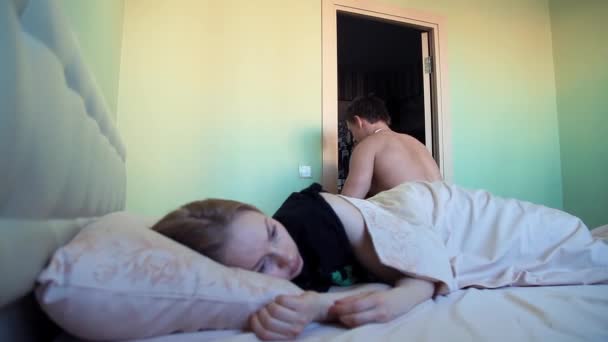 Musculoso chico se levanta de la cama por la mañana, su novia acostada bajo sábana — Vídeos de Stock