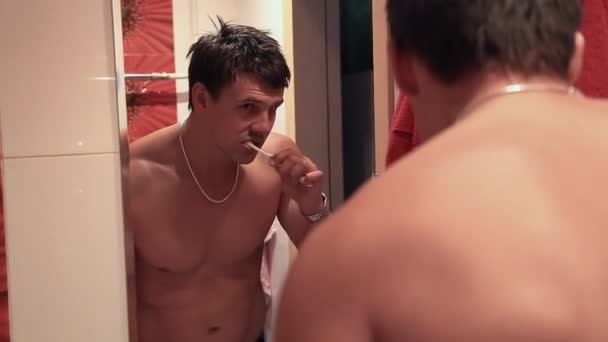 Muskulös man borstar tänderna i badrum framför spegeln — Stockvideo
