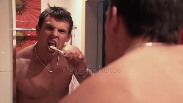 Сильный парень чистит зубы в ванной перед зеркалом — стоковое видео