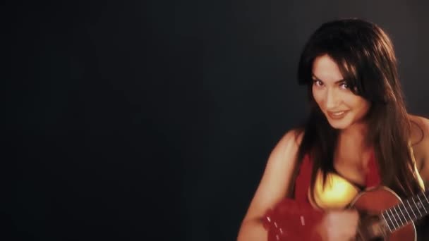 Mulher morena bonita em vestido havaiano tocando guitarra ukulele em quarto preto — Vídeo de Stock