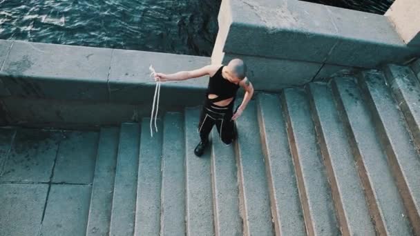 Androgyne queere Person im zerrissenen schwarzen Hemd, die Seilstücke vor der Kamera zeigt — Stockvideo