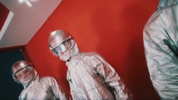 Three man in silver overalls, hard hats and goggles standing in red room — Stock Video