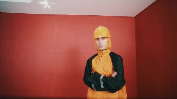 Man in hazard jacket and orange hard hat cross armed in red room, rapping — Stock Video