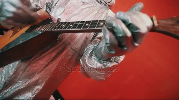 Hands in silver rubber gloves of hazard suit playing balalaika in red room — Stock Video