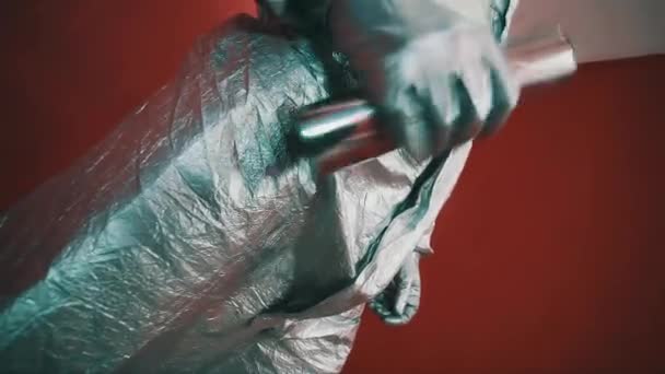 Рукавички в срібних гумових рукавичках чоловіка в небезпечному костюмі, струшуючи металевий стрижень у червоній кімнаті — стокове відео