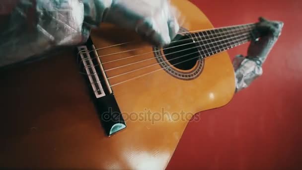 Mani in guanti di gomma argento dell'uomo in tuta di pericolo a suonare la chitarra nella stanza rossa — Video Stock