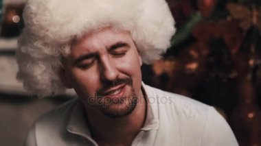 Noel süslemeleri ile odada oturan beyaz kürk şapka şarkı tıraşsız adam