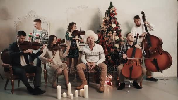 Κουιντέτο εγχόρδων με τον τραγουδιστή που παίζει μουσική στο δωμάτιο με Χριστουγεννιάτικο τοπίο — Αρχείο Βίντεο