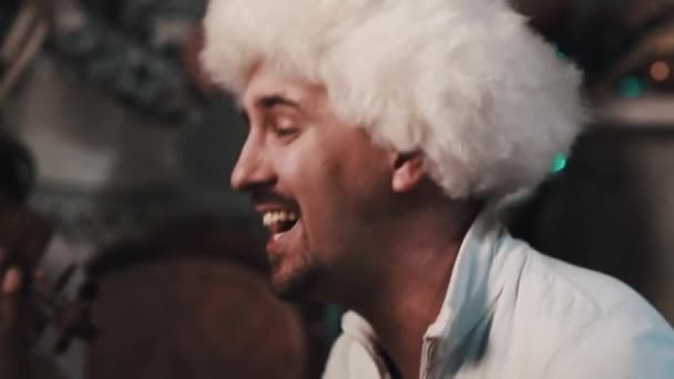 Unshaved zanger in wit bont muts zingen met strijkkwartet zit in kamer — Stockvideo