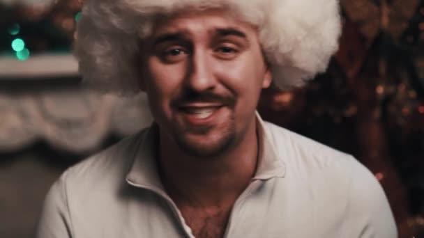 Unshaved zanger in bont muts zingen zit in kamer met kerstversiering — Stockvideo