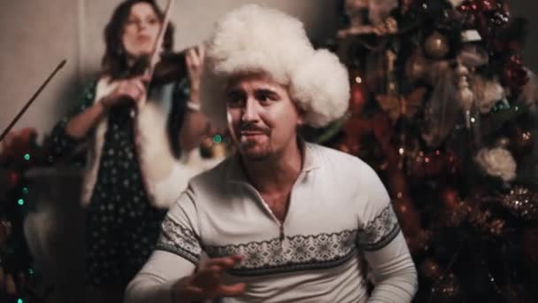 Musician in fur hat singing with string quartet sitting near christmas tree — Stock Video