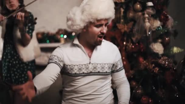 Singer in bont hoed uitvoeren met strijkkwartet zitten in de buurt van de kerstboom — Stockvideo