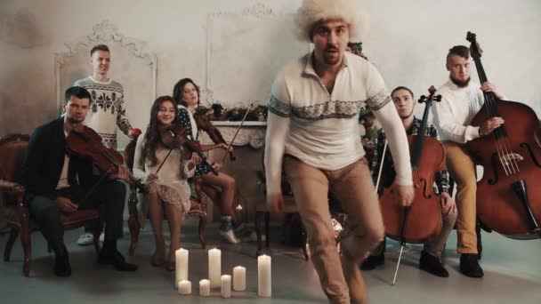 Legrační muž v klobouku bílé kožešiny zapnout fotoaparát, Smyčcový kvintet začne hrát — Stock video